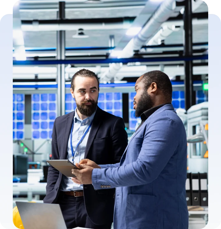WHY ORGANIZATIONS TRUST US Two business professionals discussing information on a tablet in a technology facility.